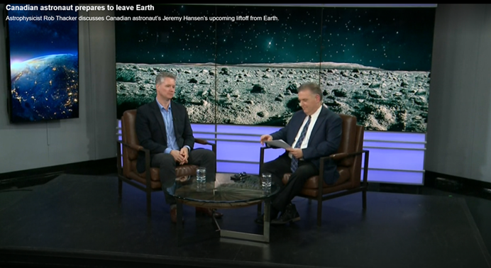 Two men sitting in chairs having a conversation on a tv set.