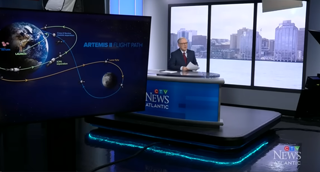 TV set, man sitting behind desk in front of window with large screen visible showing Artemis II flight path