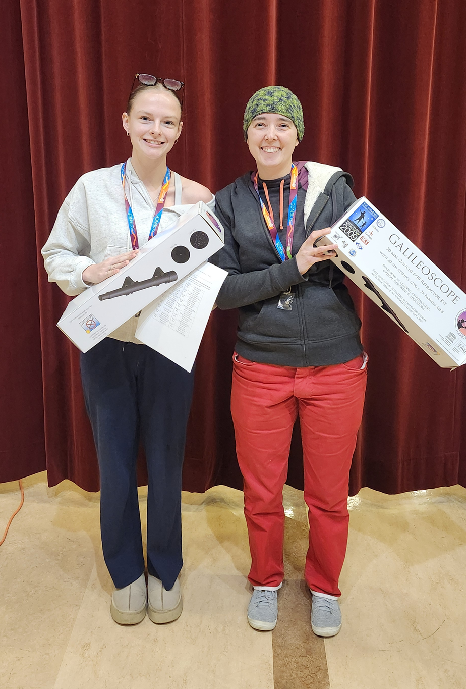 A picture of two students holding boxed telescopes