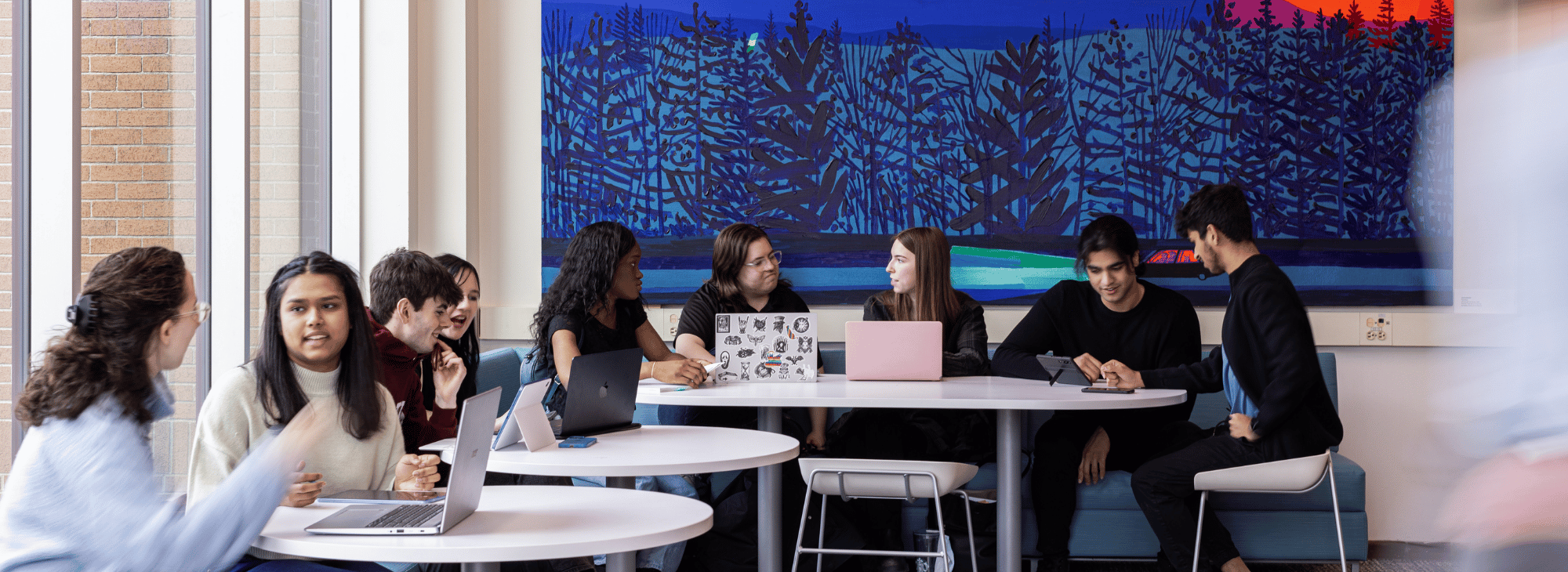 Students sit in a campus space with a colorful mural behind them