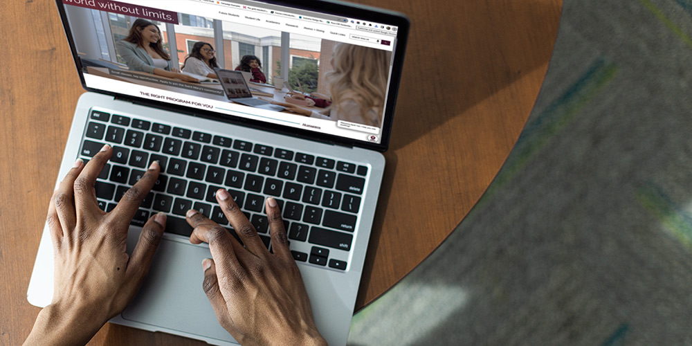 A laptop on a desk with hands on the keyboard.