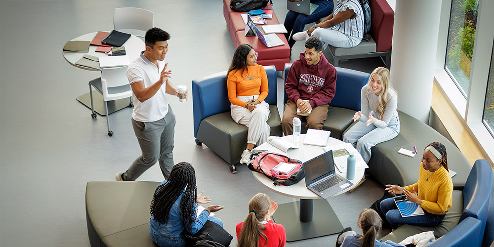 Students sit around a table smiling.