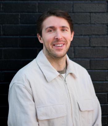 Alex Myrick posing in front of a wall with black bricks